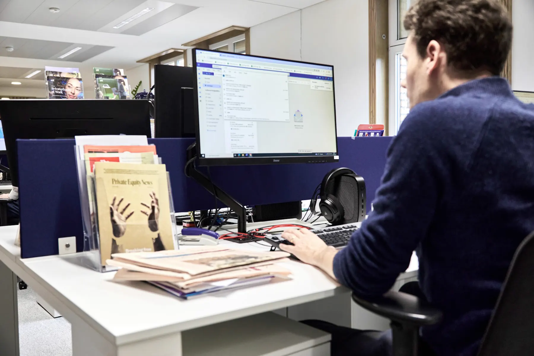 Een medewerker werkt aan een scherm op een kantoor met dossiers